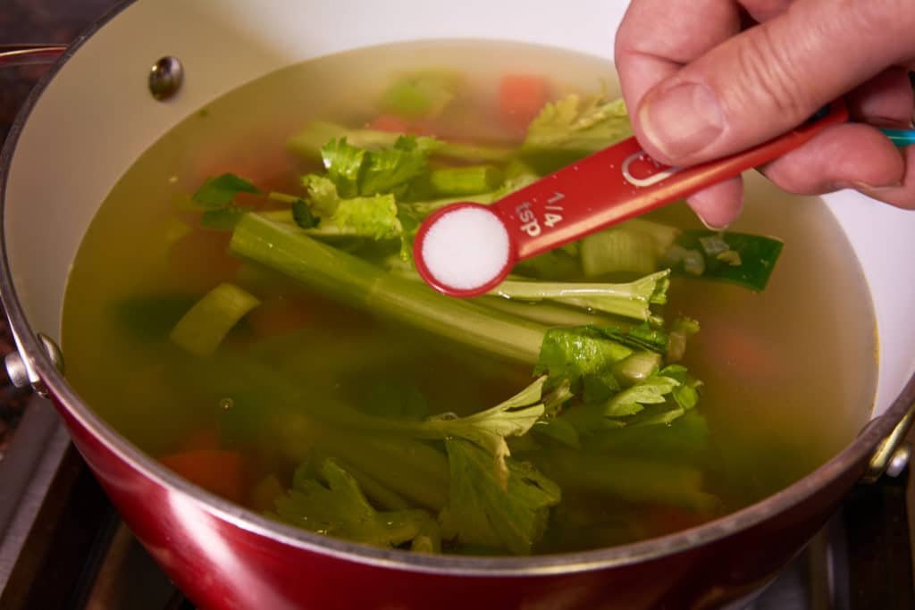 Adding salt to the pot with veggies 
