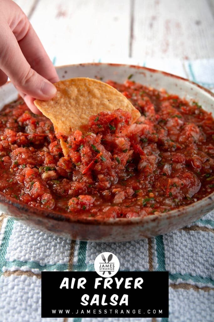 A hand dipping a chip into a bowl of air fryer salsa. This is an image for pinning to Pinterest