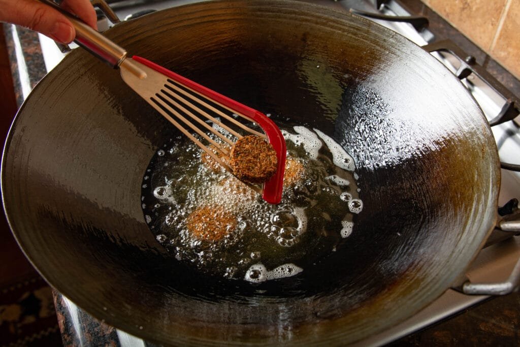 Wok with hot oil frying falafel. Holding a finished falafel on a spatula