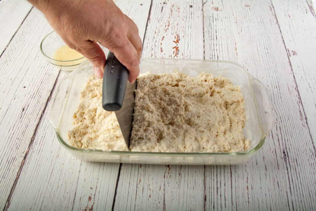A hand using a bench scraper to portion out the dough
