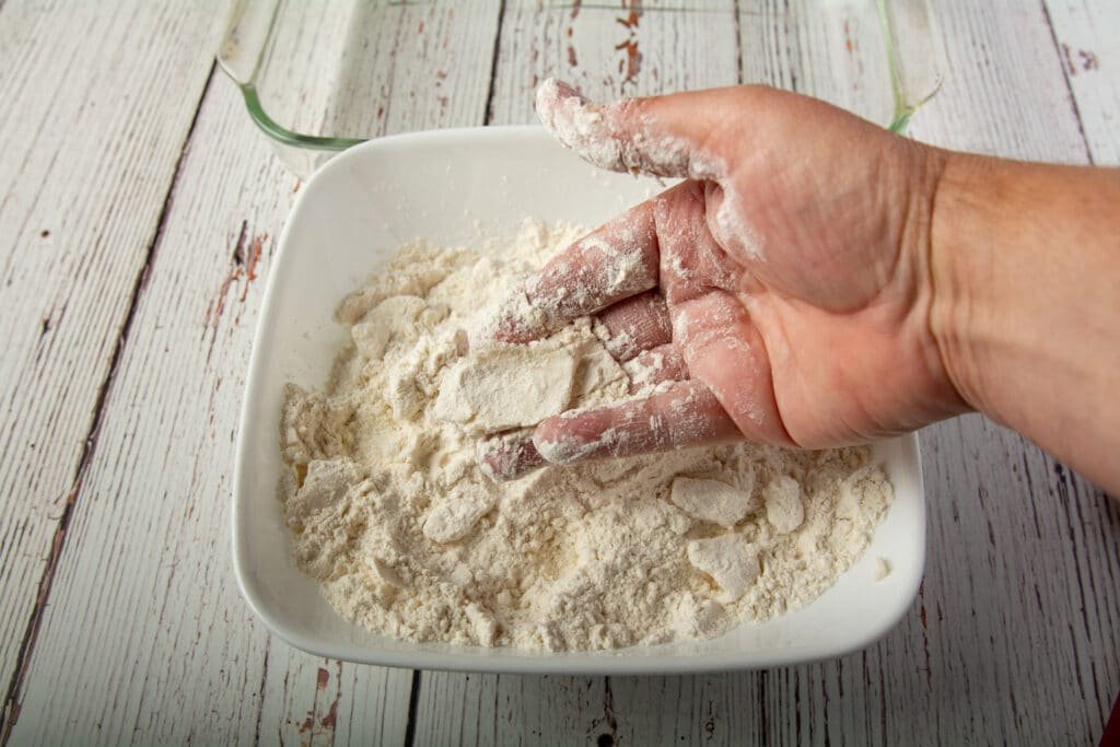A hand showing how to crumble the vegan butter into the flour.