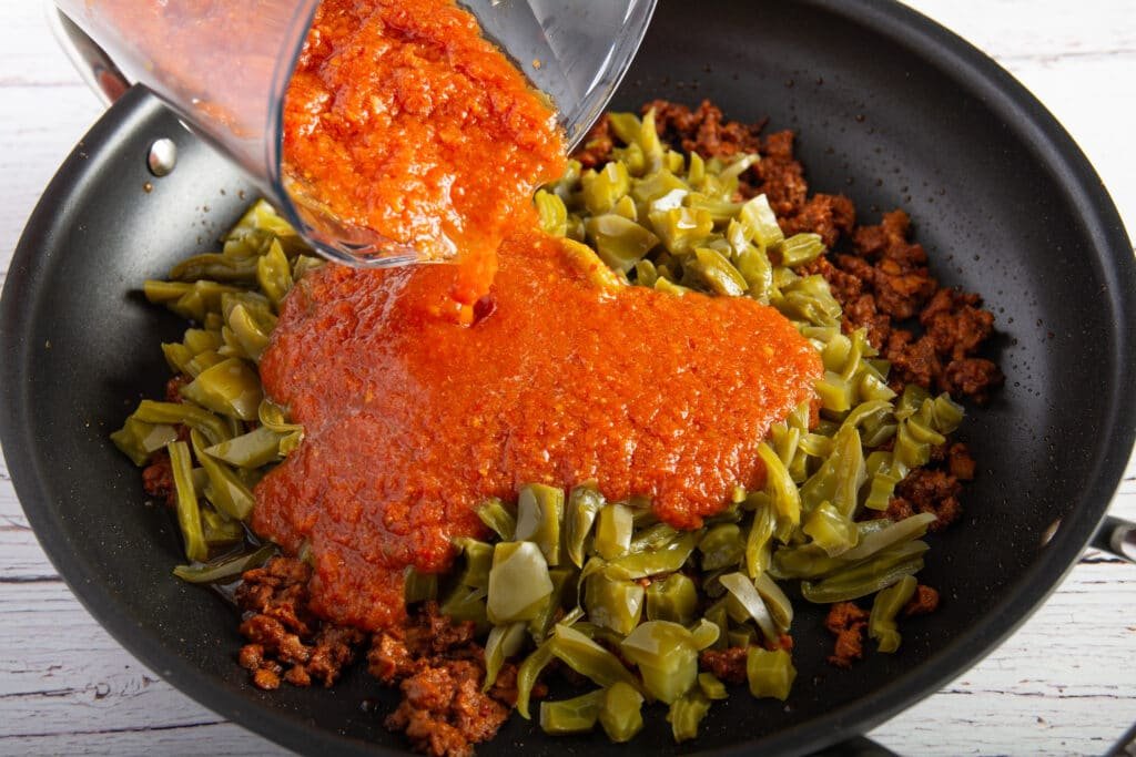 Pouring salsa into a pan with the chorizo and nopales
