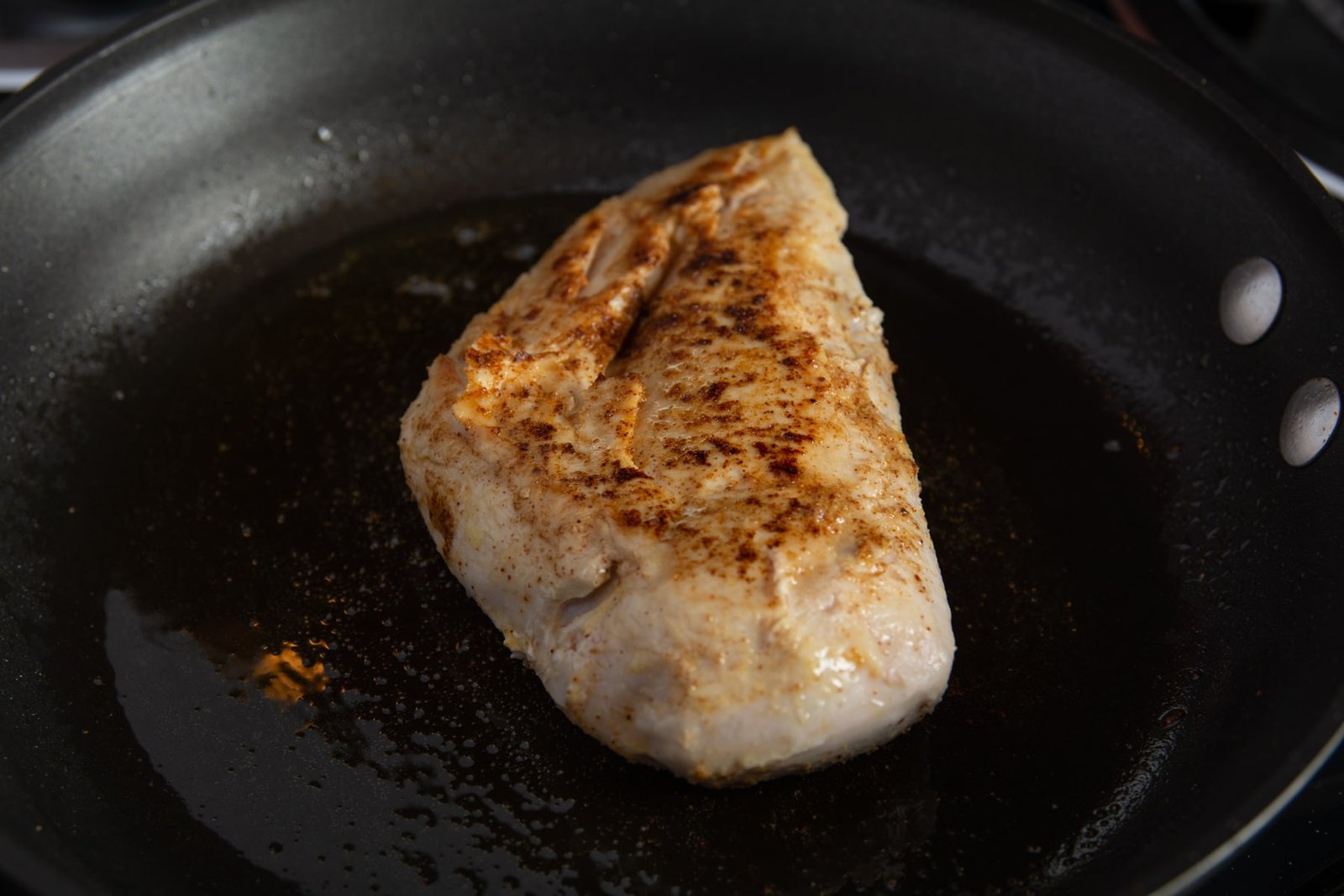 Chicken breast in a pan with the top side seared.