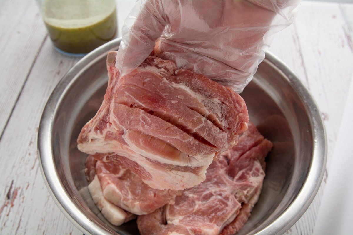 A bowl with pork steaks. A hand holding one of the steaks showing the cuts.