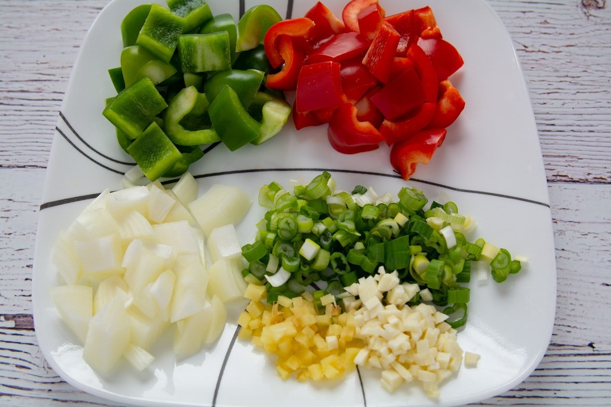 Ginger, garlic, onions, and bell peppers cut up and on a plate