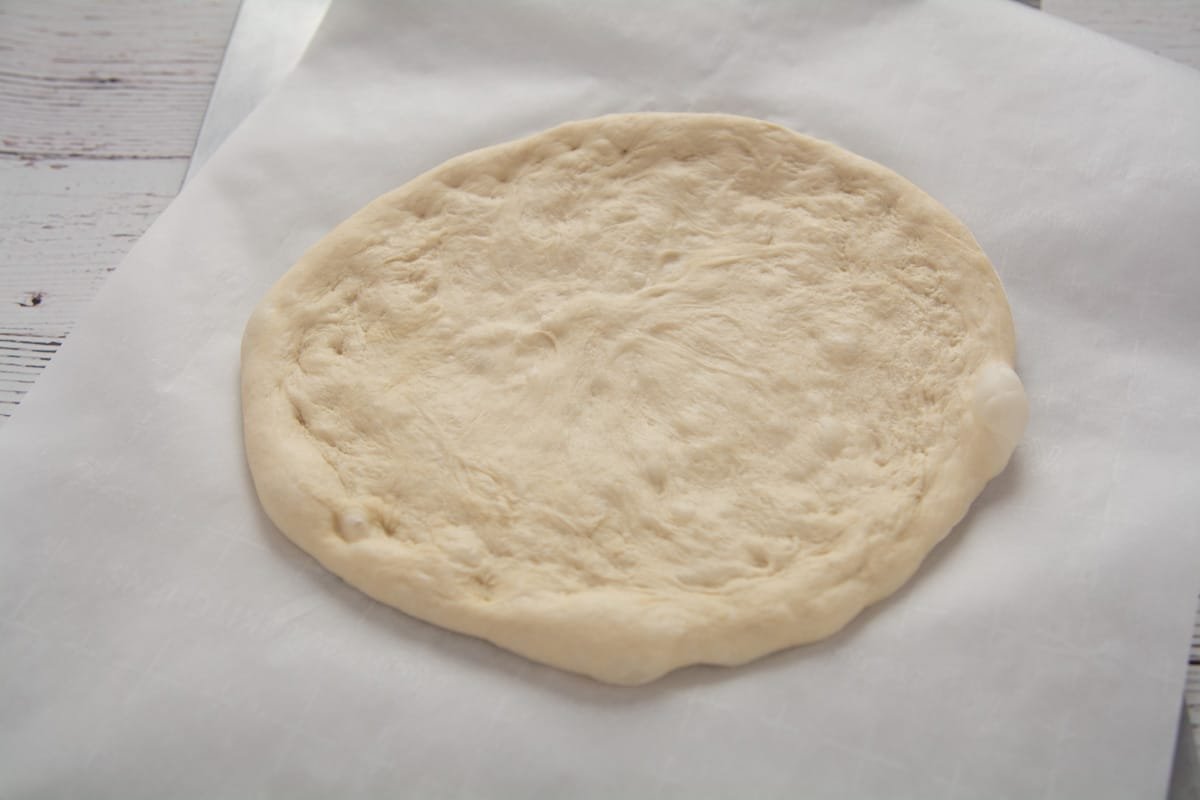 Pizza dough stretched out and formed into a pizza on parchment paper.