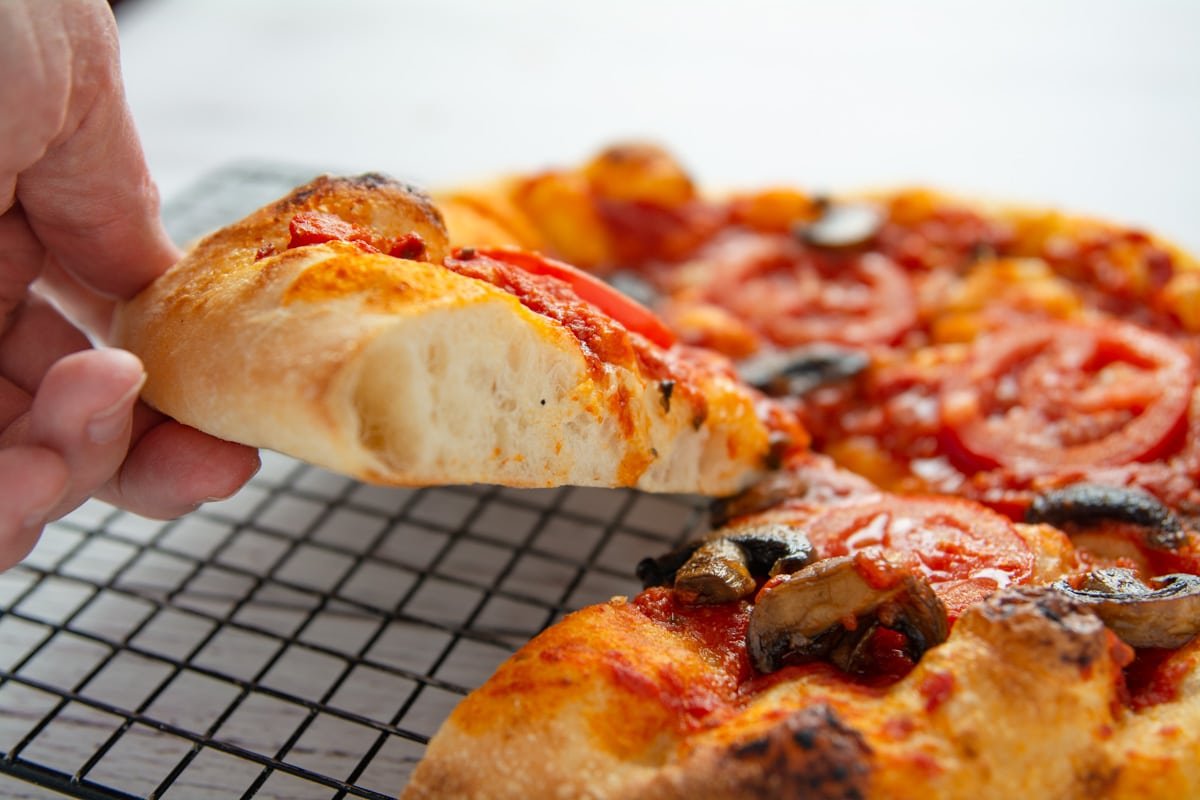 A hand lifting a slice of pizza showing the air pockets in the vegan crust.