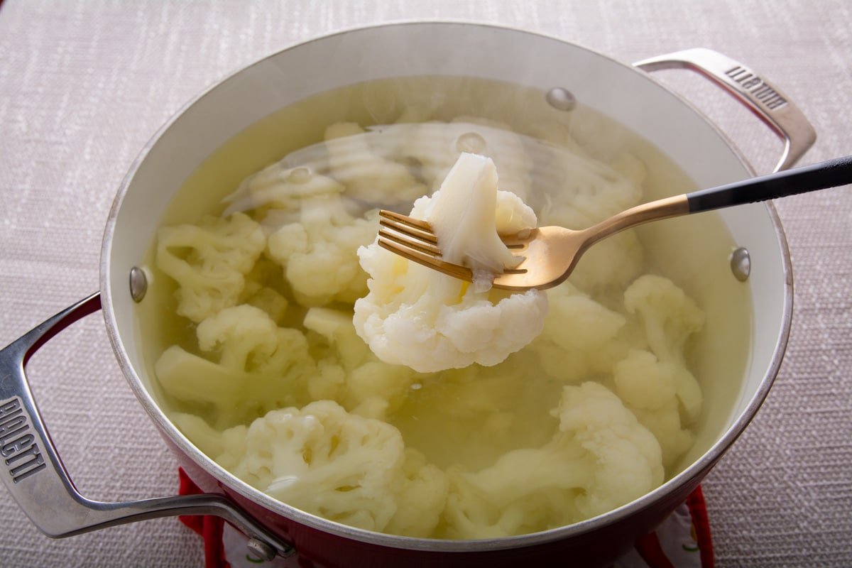 A fork holding cooked cauliflower over a pot of cooked cauliflower.