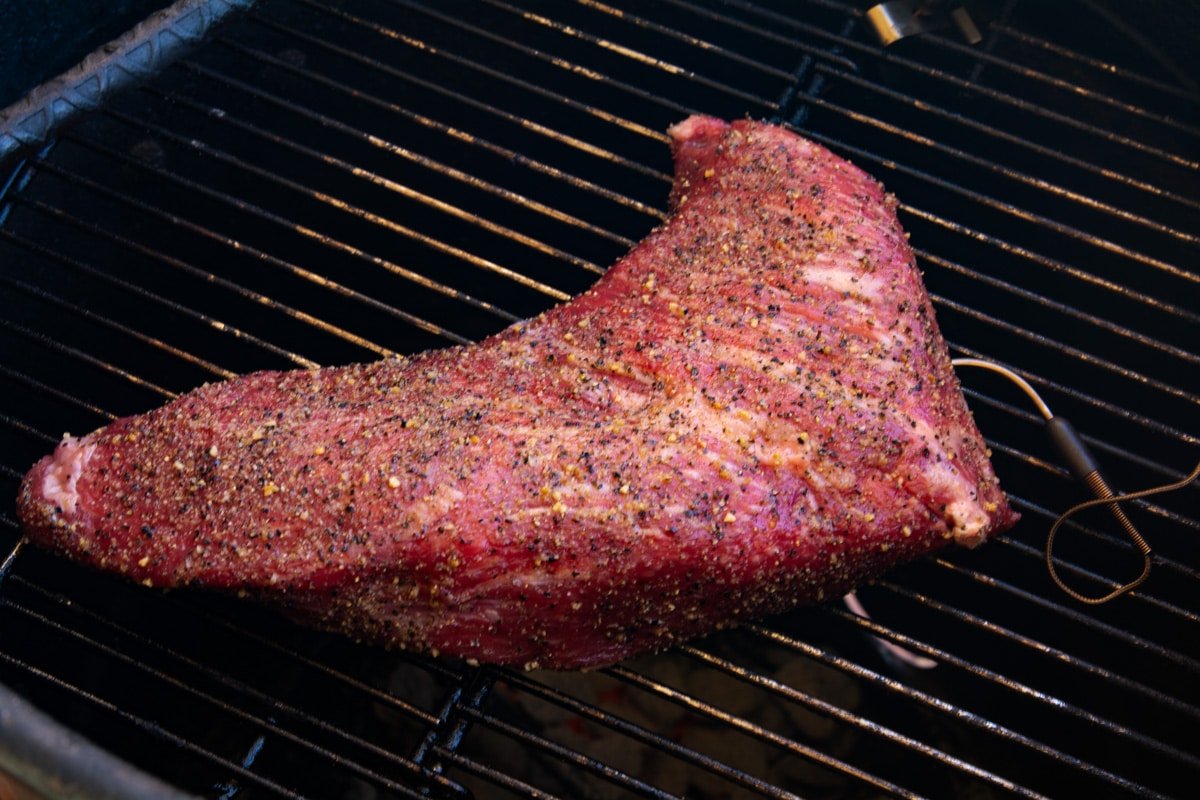 Raw, seasoned tri tip on a grill with a thermometer