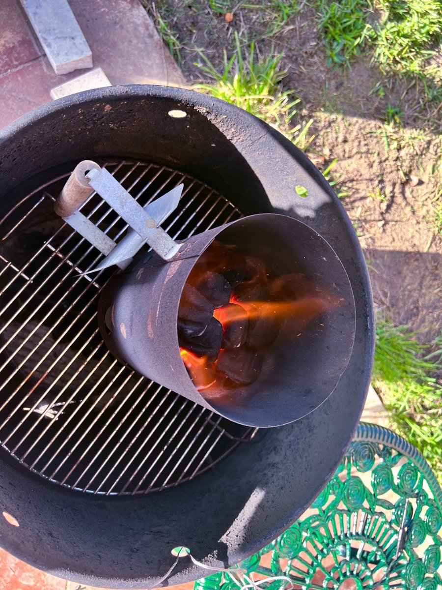 A Charcoal chimney on a grill with burning charcoal.