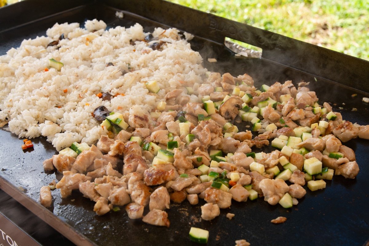 Chicken veggies and rice cooking on a griddle.