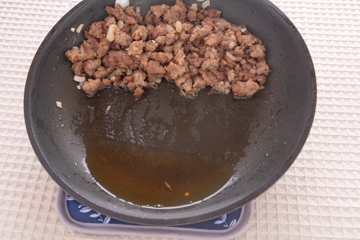 Pan with browned sausage. Pan is tilted to drain the oil.