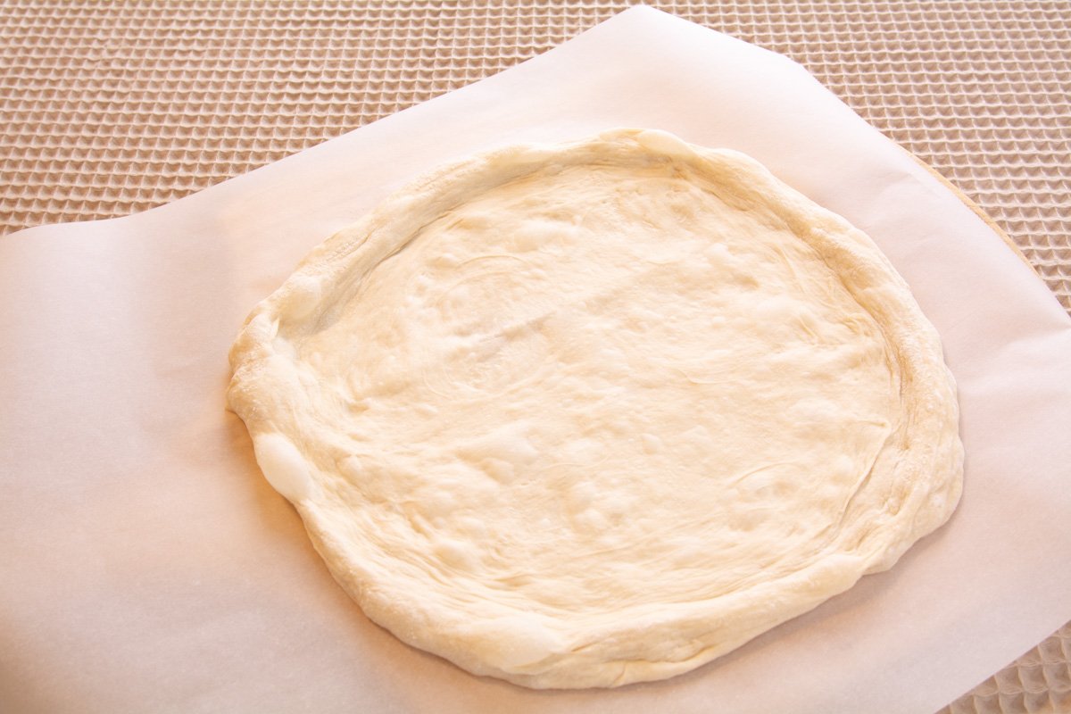 Poolish dough spread out into a round shape ready for topping.