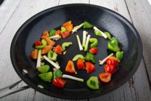 Bell peppers, green onion, garlic and ginger in a pan on a table.