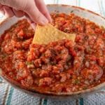 A hand dipping a chip into a bowl of air fryer salsa.