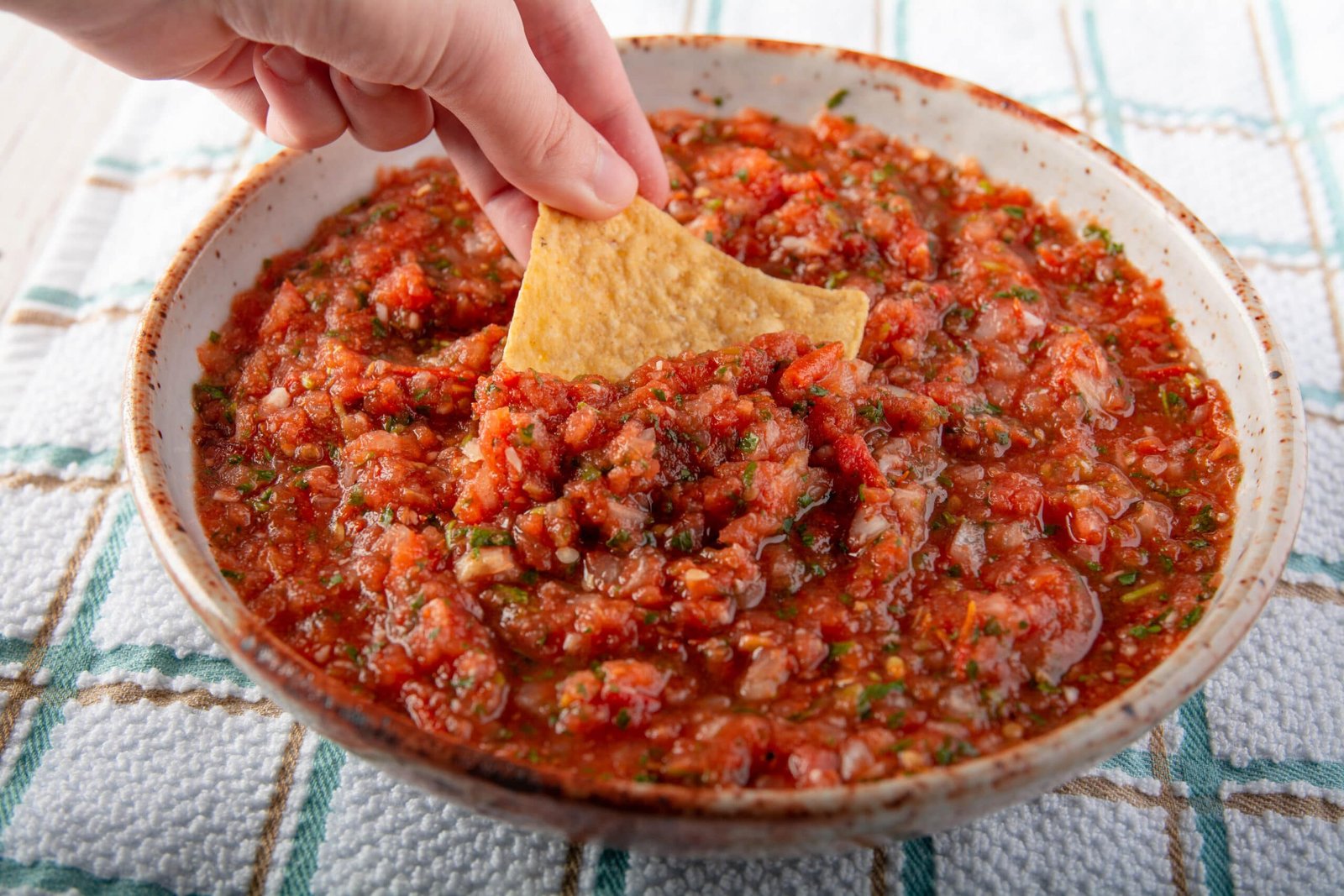 A hand dipping a chip into a bowl of air fryer salsa.
