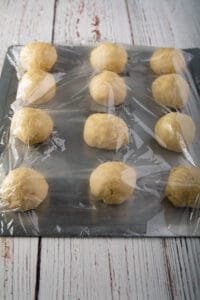 Balls of dough on a cookie sheet covered with plastic wrap