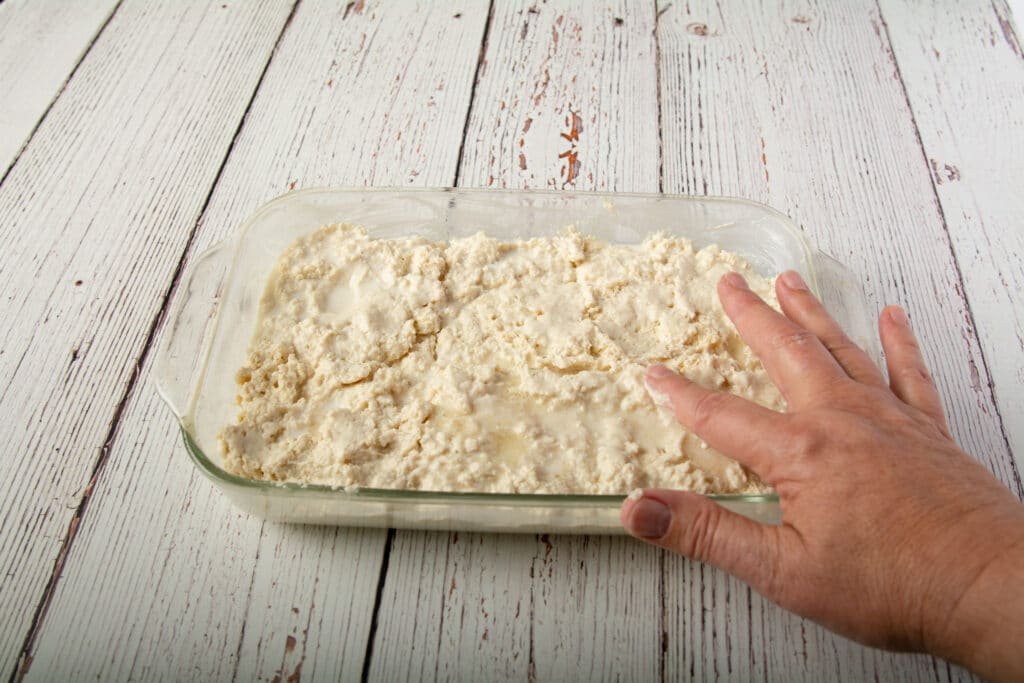 A hand smoothing the top of the vegan biscuit dough
