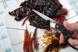 Dried chilis on a plate. Using scissors to cut one on the chilis