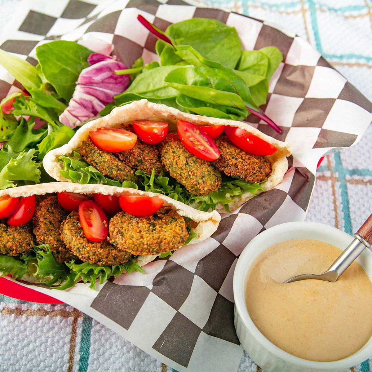 Falafel sandwich in a basket with sauce on the side