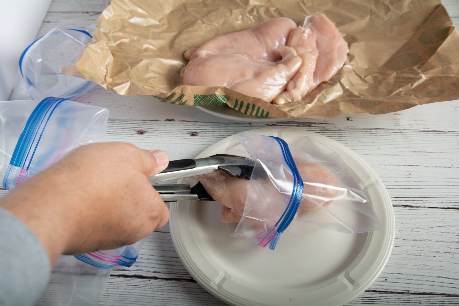 Using tongs to put raw chicken breast in a bag.