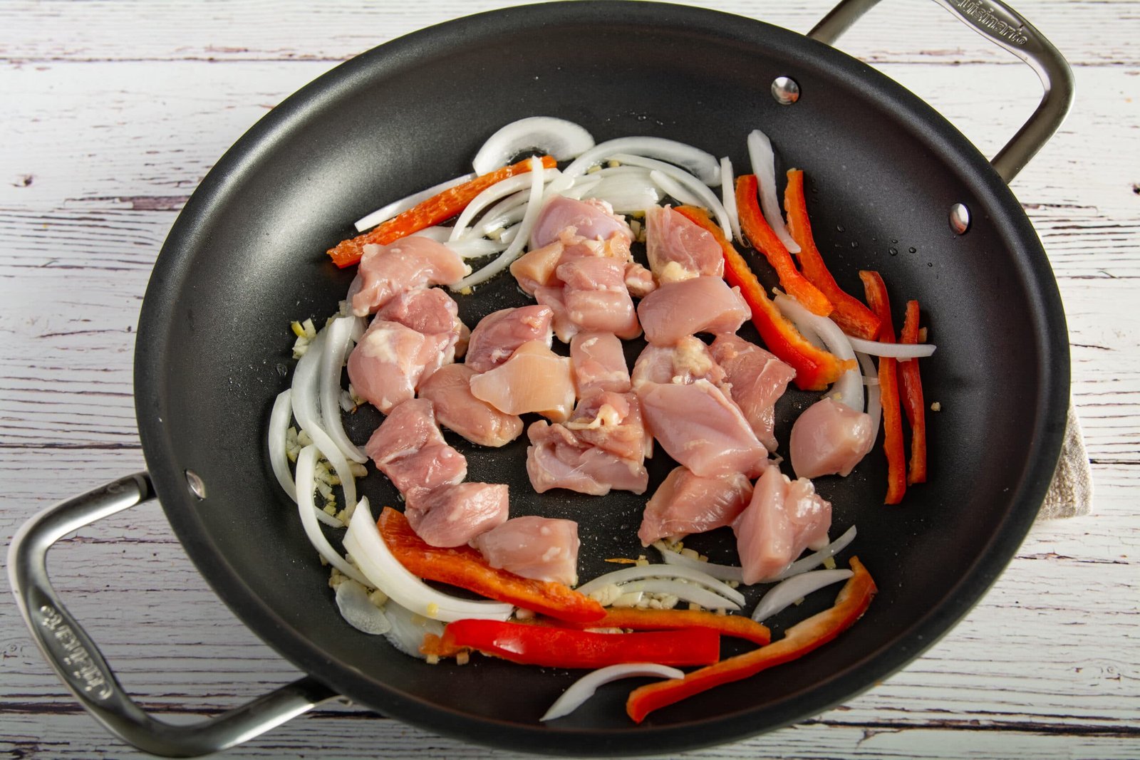 Raw chicken in a pan with onions and bell peppers