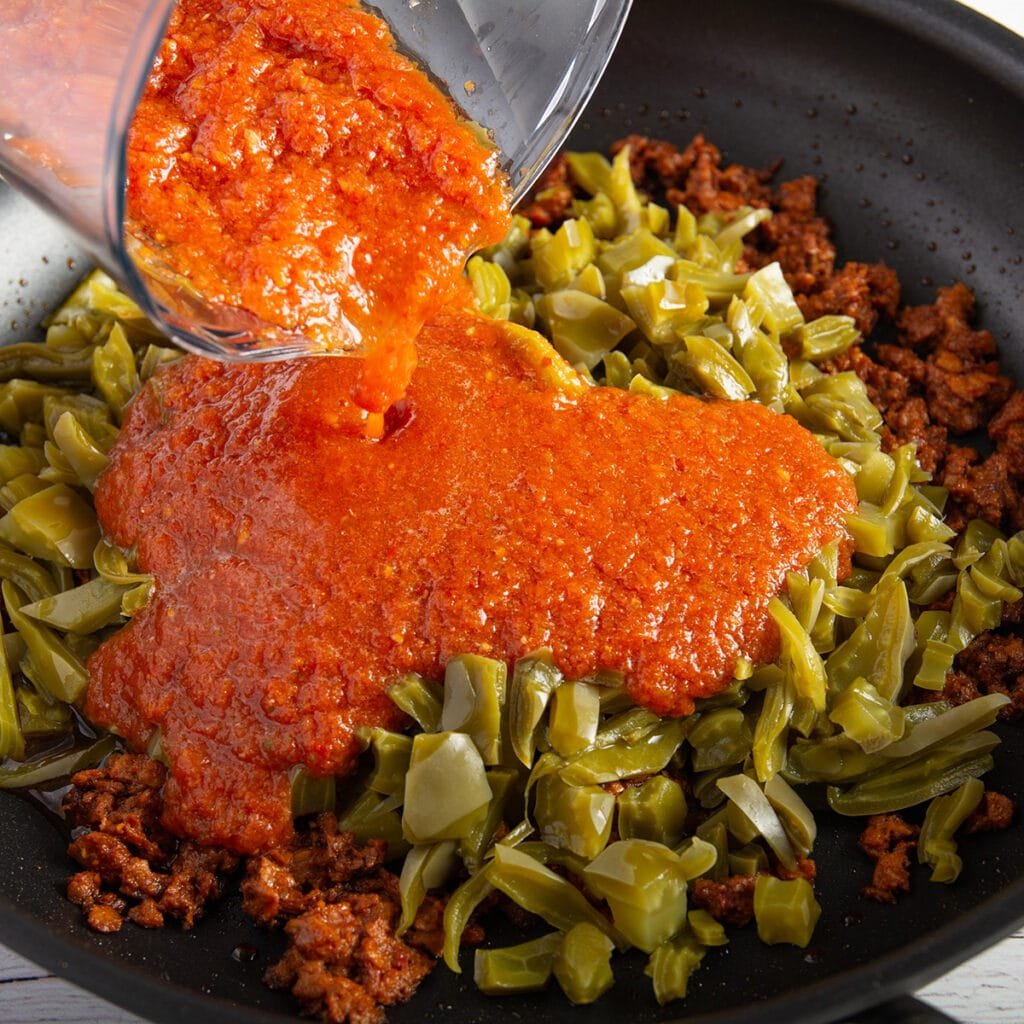 Pouring salsa into a pan with the chorizo and nopales