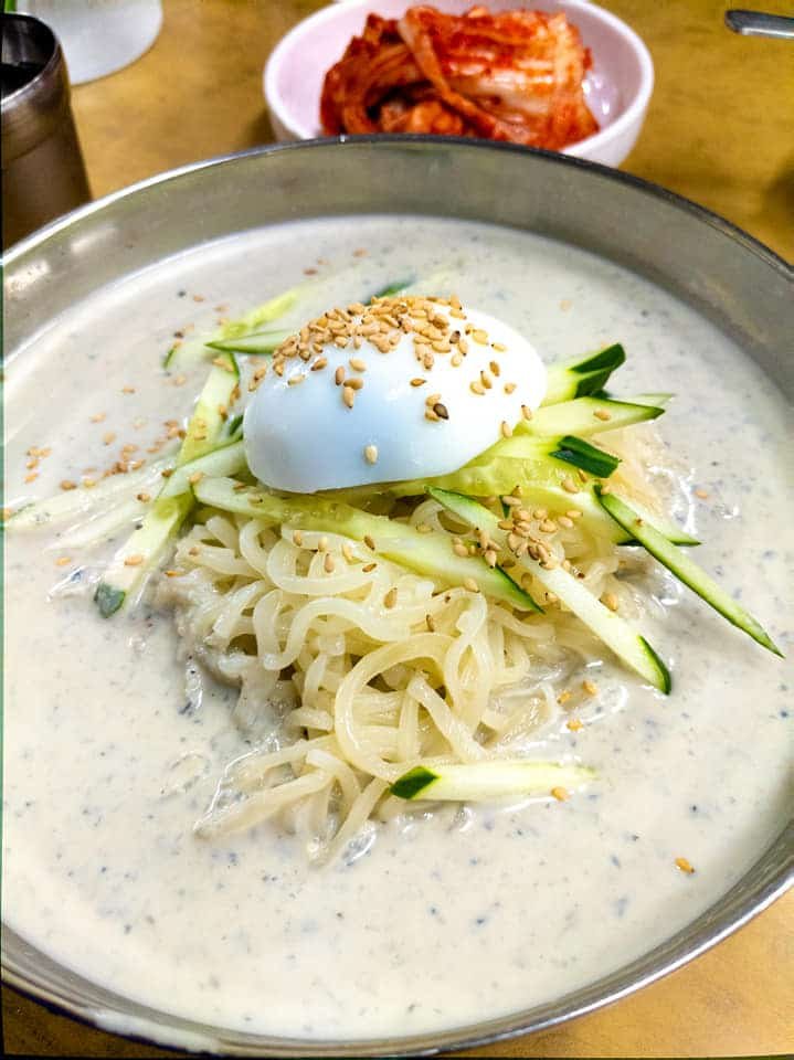 Small thin noodles in soy milk soup in a bowl with an egg on top.
