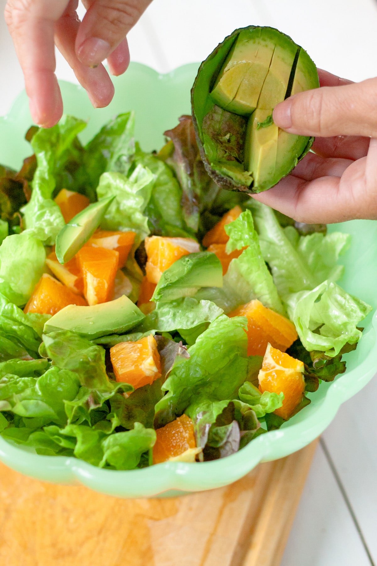 A bowl of salad with a hand sprinkling on chunks of avocado