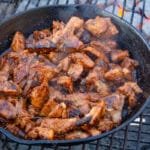 Spicy pork in a cast iron pan cooking on a grill.