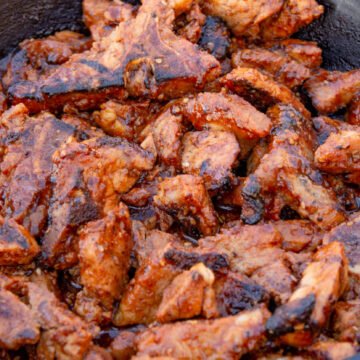 Spicy pork in a cast iron pan cooking on a grill.