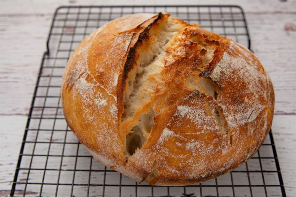 A loaf of sourdough bread cooling on a rack