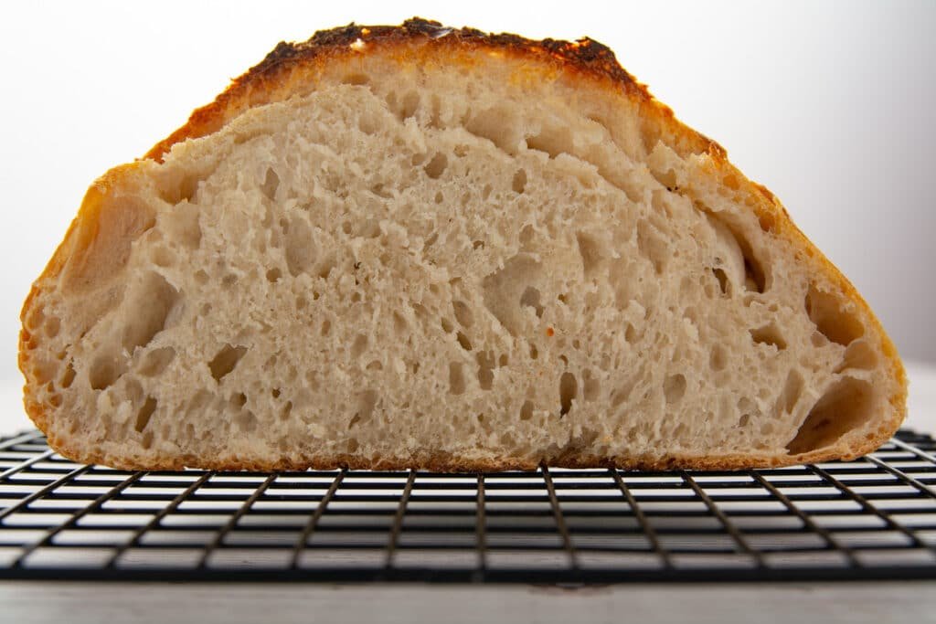 A loaf of sourdough bread cut in half cooling on a rack
