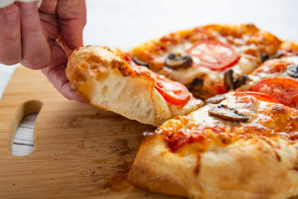 A hand lifting a slice of pizza showing the air pockets in the regular crust.