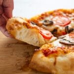 A hand lifting a slice of pizza showing the air pockets in the regular crust.