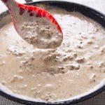 A spoon dipping white gravy in a pan