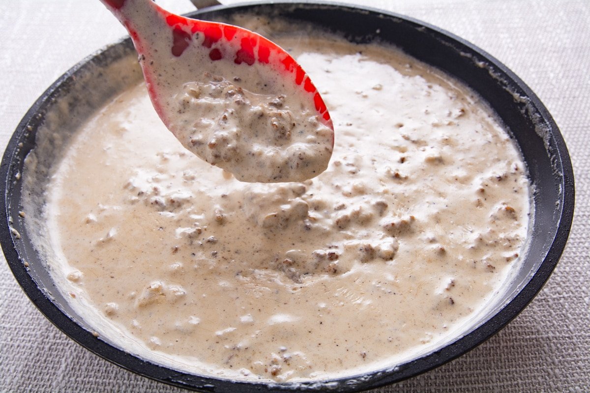 A spoon dipping white gravy in a pan