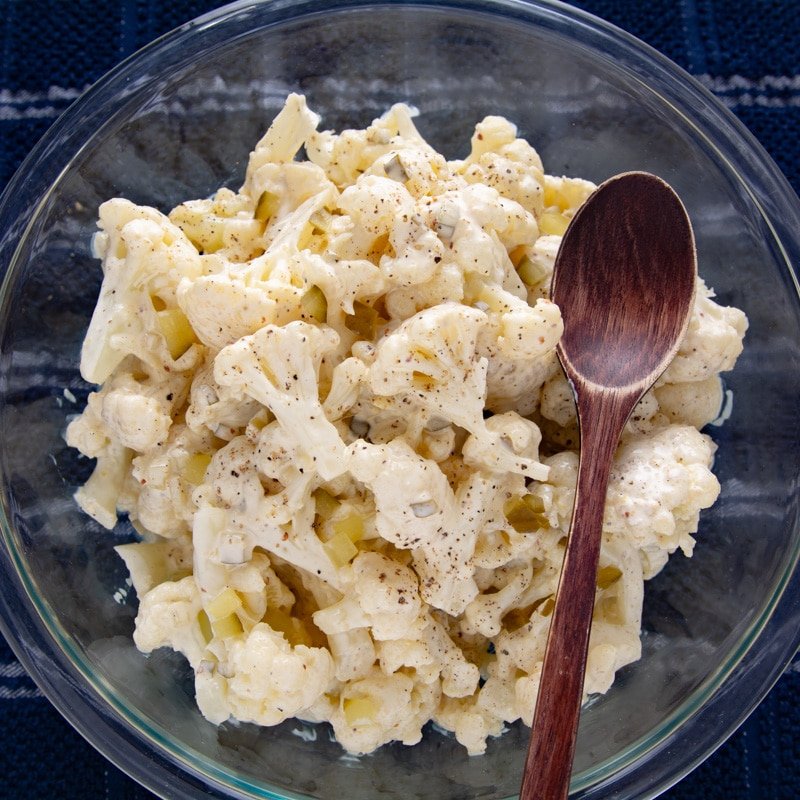Cauliflower potato salad in a bowl with a wooden spoon.