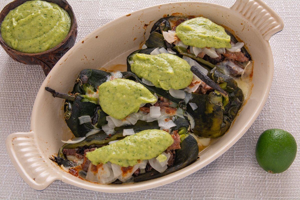 Cooked chili rellenos with green salsa in a pan