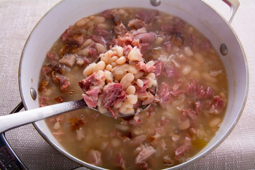 Finished navy beans with ham in a pot and a ladle.