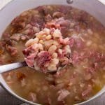 Finished navy beans with ham in a pot and a ladle.
