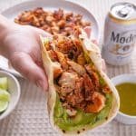 Hand holding a chicken taco with guacamole.