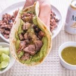 A hand holding a carne asada taco with guacamole