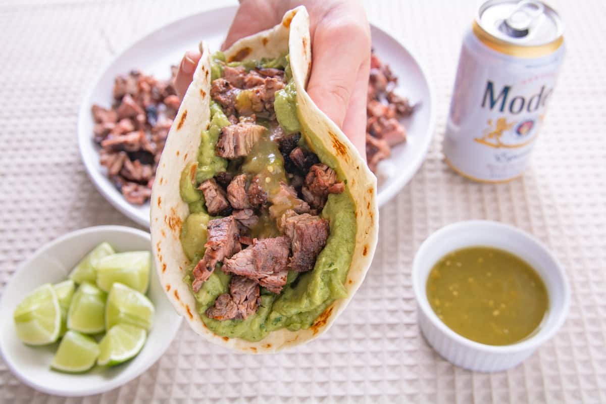 A hand holding a carne asada taco with guacamole