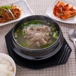 Table setting of oxtail soup, rice, kimchi and seasoned meat.