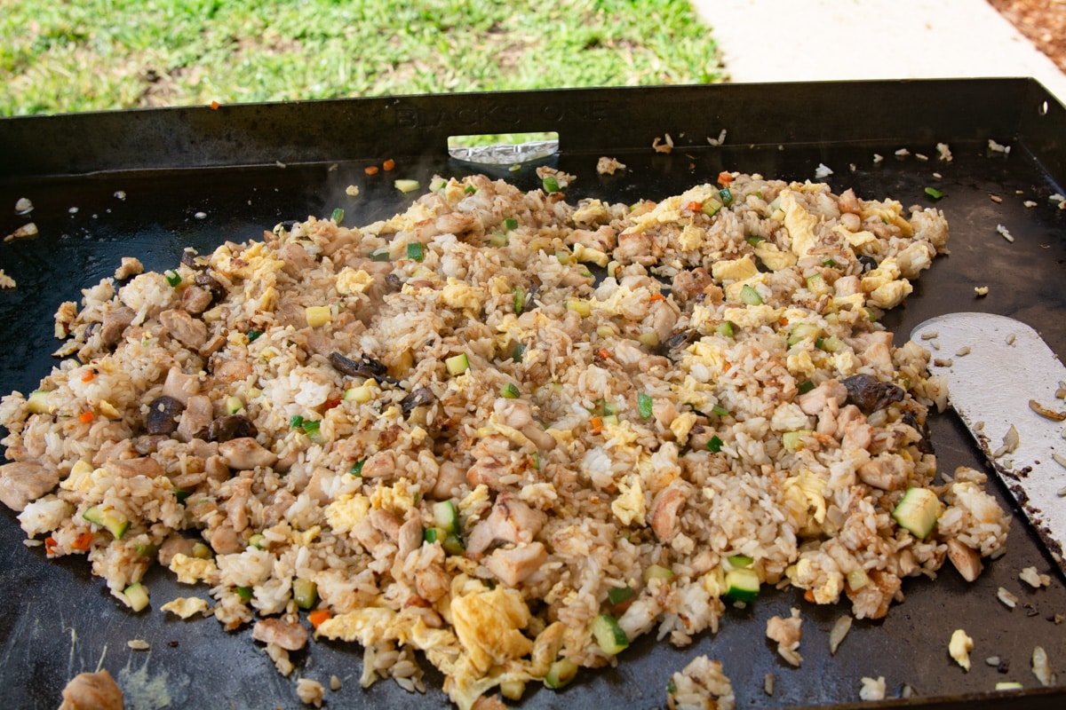 Chicken veggies and rice cooking on a griddle.