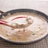 Pan of white gravy with a spoon dipping some gravy.