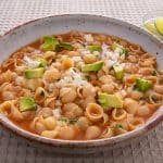 Finished bowl of sopa with shells on a table with a small bowl of lime slices.