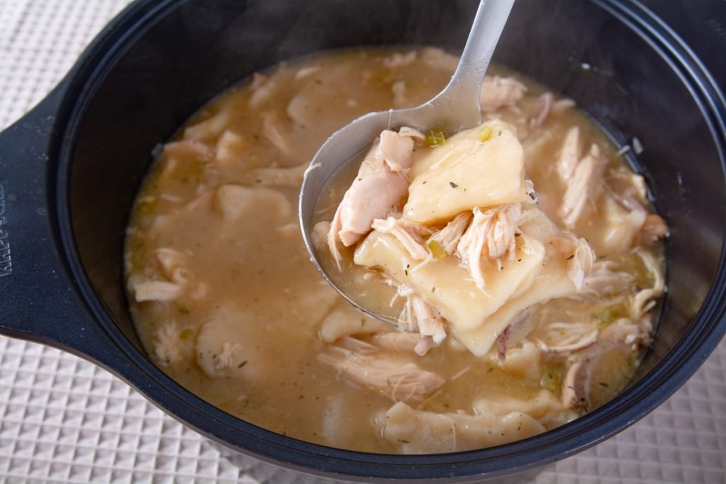 A ladle scoping chicken and dumplings from a pot.