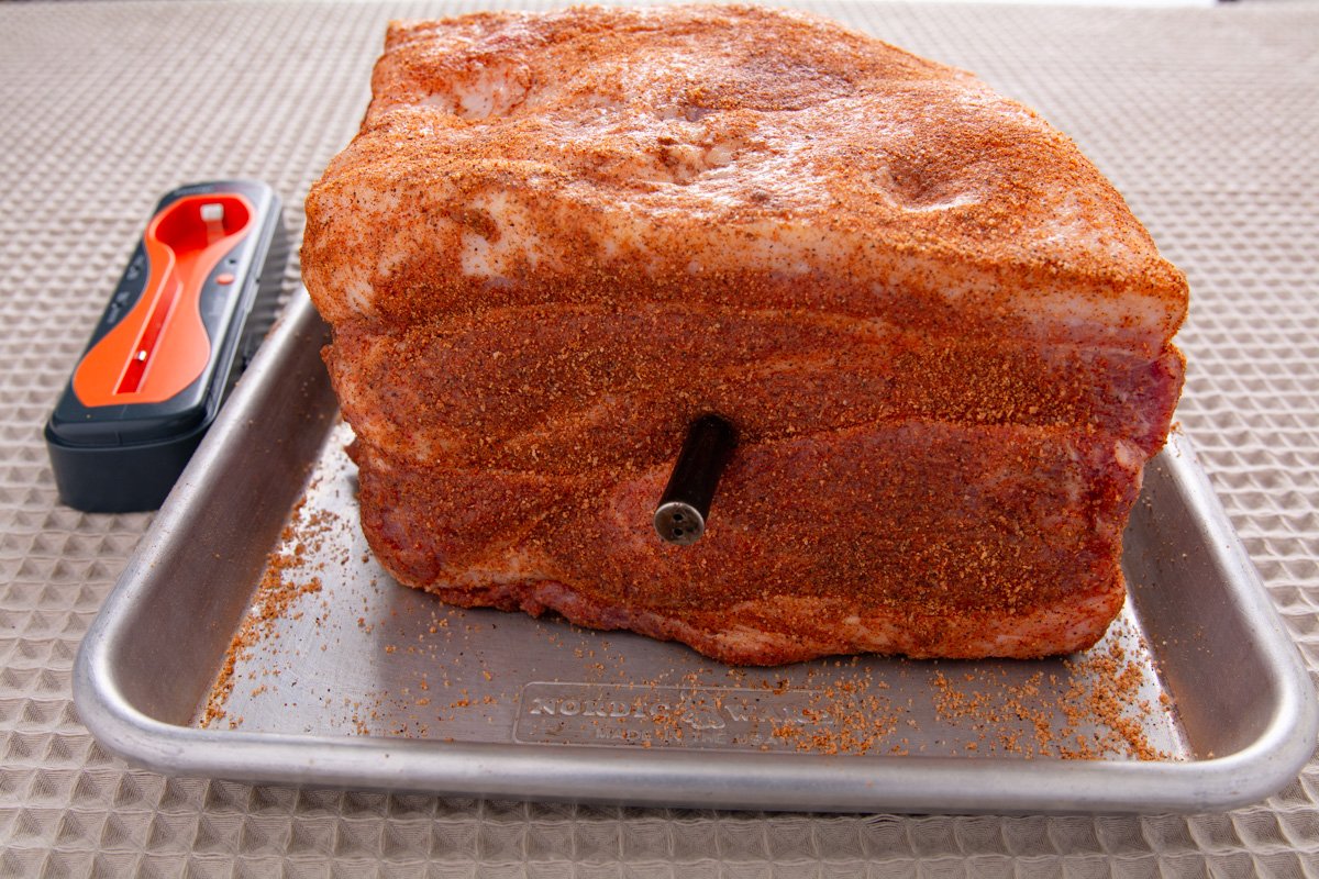 Seasoned raw pork butt on a baking tray with a thermometer inserted.